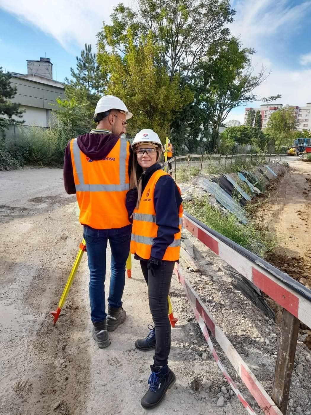 Mariana Garștea și un coleg, în veste Sixense, lângă un trepied topografic pe marginea unei excavații